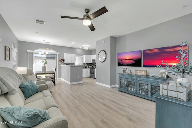 living room with light wood finished floors, baseboards, visible vents, and ceiling fan with notable chandelier