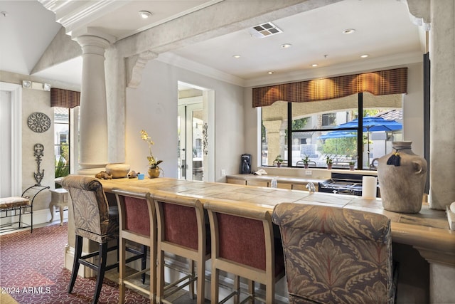 kitchen featuring a kitchen bar, carpet, decorative columns, and crown molding