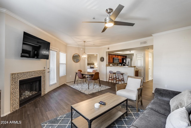 living room featuring dark hardwood / wood-style flooring, ceiling fan with notable chandelier, crown molding, and a tiled fireplace