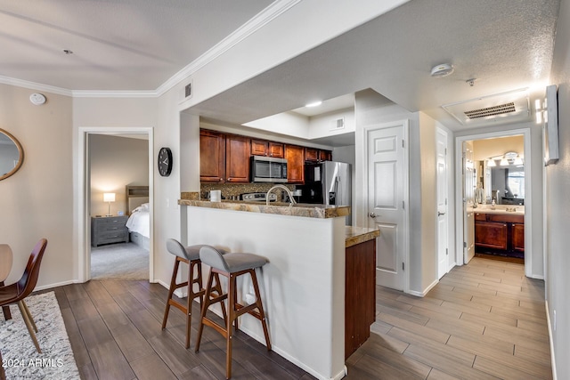 kitchen with kitchen peninsula, tasteful backsplash, ornamental molding, a breakfast bar, and stainless steel appliances