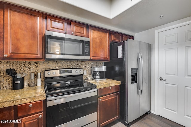 kitchen with decorative backsplash, dark hardwood / wood-style flooring, light stone counters, and appliances with stainless steel finishes