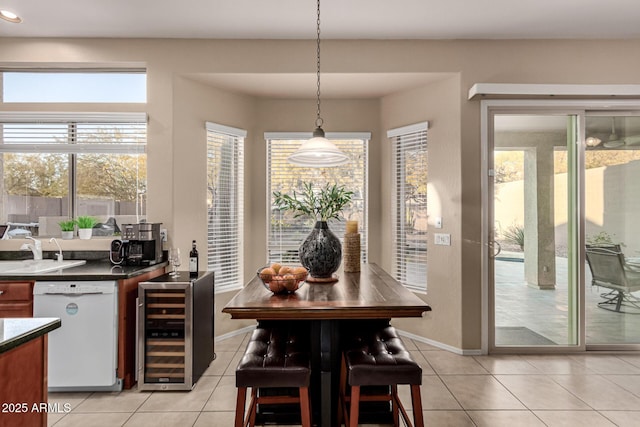 kitchen featuring pendant lighting, sink, light tile patterned floors, white dishwasher, and beverage cooler