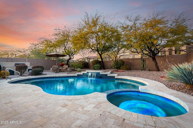 pool at dusk with a patio, pool water feature, and an in ground hot tub