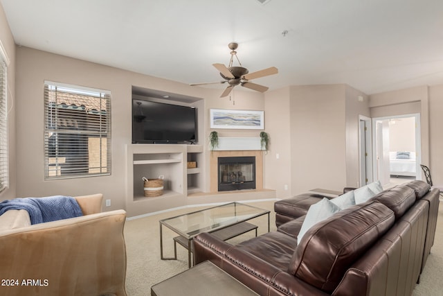 living room featuring a tiled fireplace, carpet floors, ceiling fan, and built in features