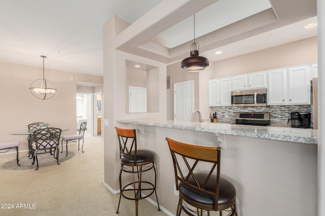 kitchen featuring light colored carpet, hanging light fixtures, light stone counters, and backsplash