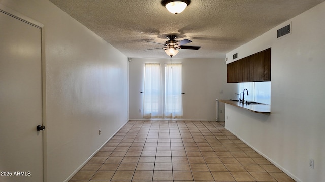 spare room with visible vents, a ceiling fan, light tile patterned flooring, a sink, and a textured ceiling