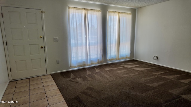 carpeted spare room with baseboards, a textured ceiling, and tile patterned floors