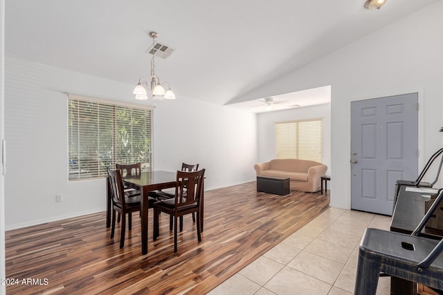 tiled dining space featuring ceiling fan with notable chandelier and vaulted ceiling