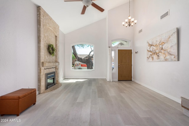 foyer entrance with ceiling fan with notable chandelier, a fireplace, light wood-type flooring, and high vaulted ceiling