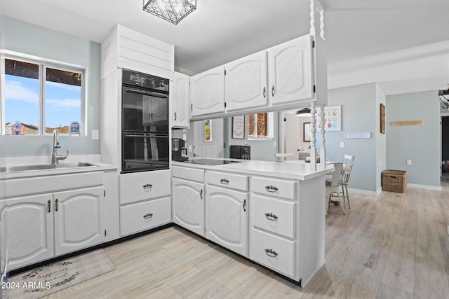 kitchen featuring light hardwood / wood-style floors, sink, kitchen peninsula, black appliances, and white cabinetry