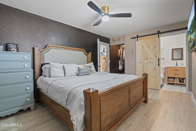 bedroom featuring a closet, a spacious closet, light wood-type flooring, ensuite bath, and a barn door