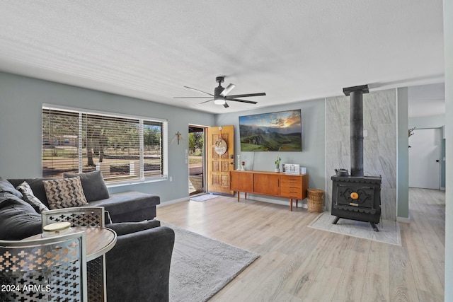 living room featuring ceiling fan, light hardwood / wood-style flooring, a textured ceiling, and a wood stove