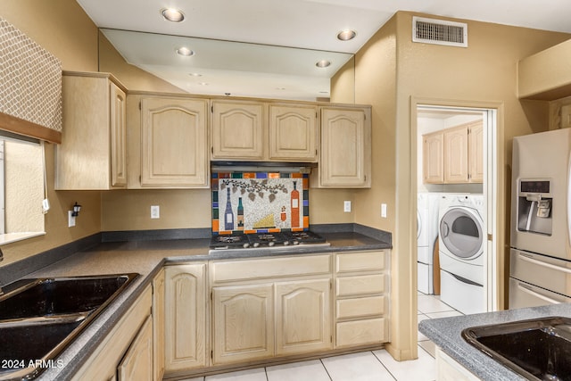 kitchen with sink, appliances with stainless steel finishes, light brown cabinetry, light tile patterned floors, and washing machine and clothes dryer