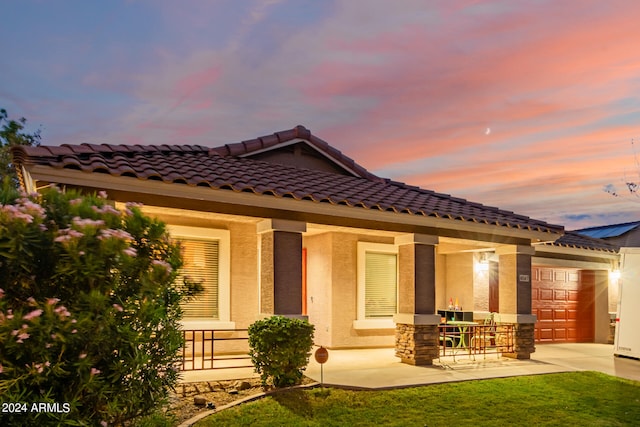 back house at dusk with a garage and a yard