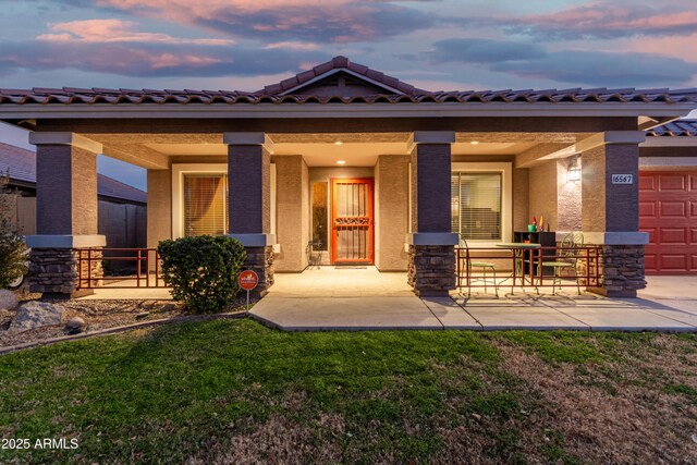 view of front of house featuring a garage, covered porch, and a lawn