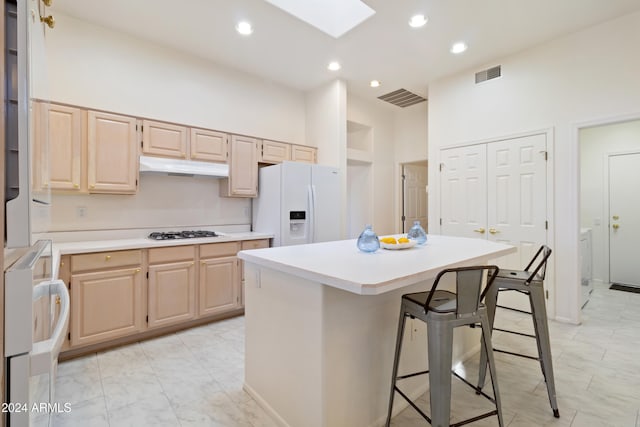 kitchen with a breakfast bar, light brown cabinetry, a skylight, white appliances, and a center island