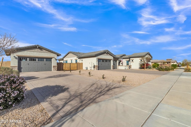 ranch-style home featuring decorative driveway, stone siding, fence, and stucco siding