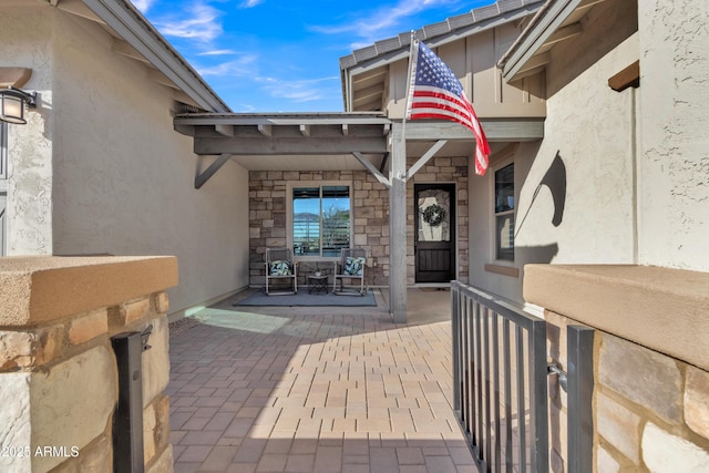 view of exterior entry with covered porch, stone siding, and stucco siding