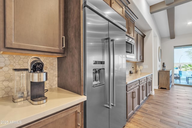 kitchen featuring light wood finished floors, decorative backsplash, built in appliances, light countertops, and beam ceiling