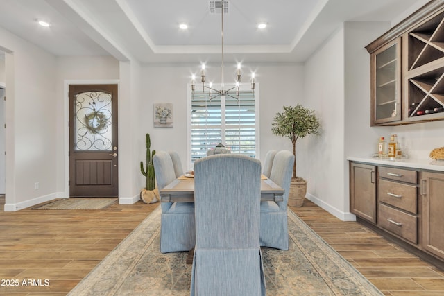 dining space featuring visible vents, a raised ceiling, baseboards, an inviting chandelier, and wood tiled floor