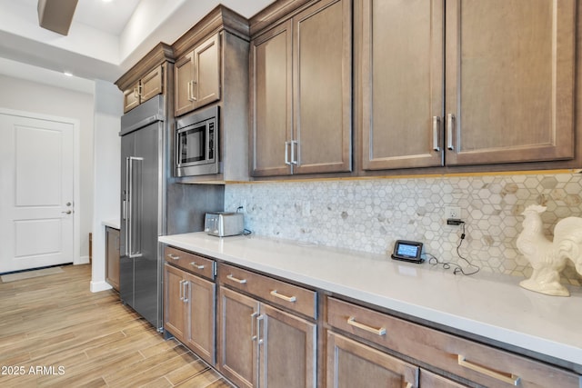 kitchen with light wood finished floors, tasteful backsplash, light countertops, and built in appliances