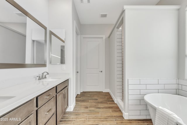 bathroom featuring double vanity, visible vents, a freestanding bath, wood tiled floor, and a sink