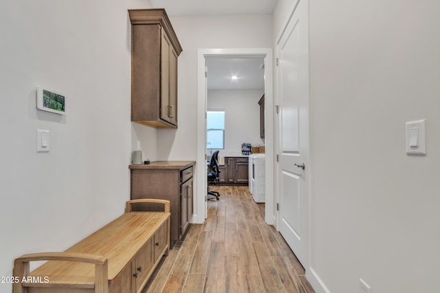 corridor with light wood-style floors and washer / dryer