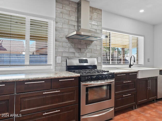 kitchen featuring decorative backsplash, dark brown cabinetry, wall chimney exhaust hood, sink, and stainless steel gas range