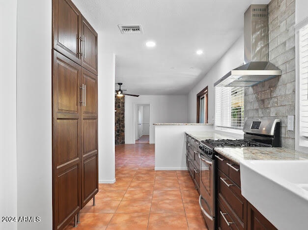 kitchen featuring light tile patterned flooring, ceiling fan, wall chimney exhaust hood, and gas range