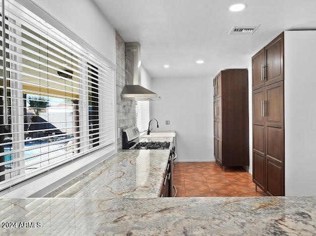 kitchen with light stone counters, stainless steel gas range, sink, tile patterned flooring, and wall chimney exhaust hood