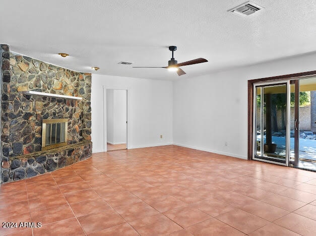 unfurnished living room with ceiling fan, a stone fireplace, and a textured ceiling