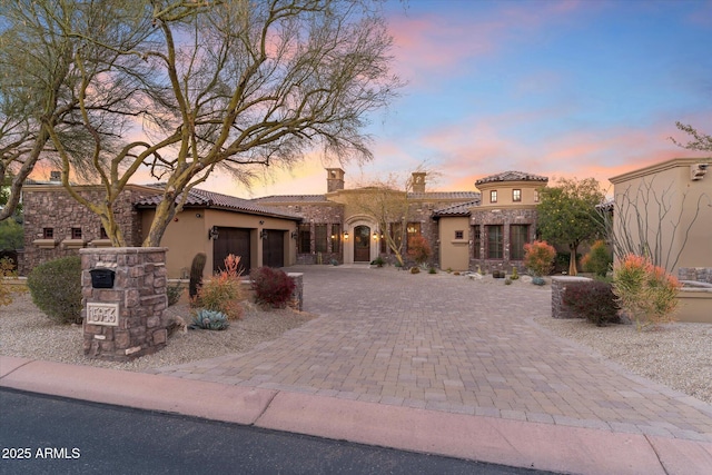 mediterranean / spanish home featuring stucco siding, a tile roof, decorative driveway, stone siding, and a garage