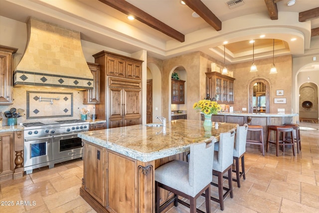 15956 E Tombstone Trl, Fountain Hills, AZ 85268 - kitchen featuring stone tile floors, brown cabinetry, custom exhaust hood, range with two ovens, and arched walkways