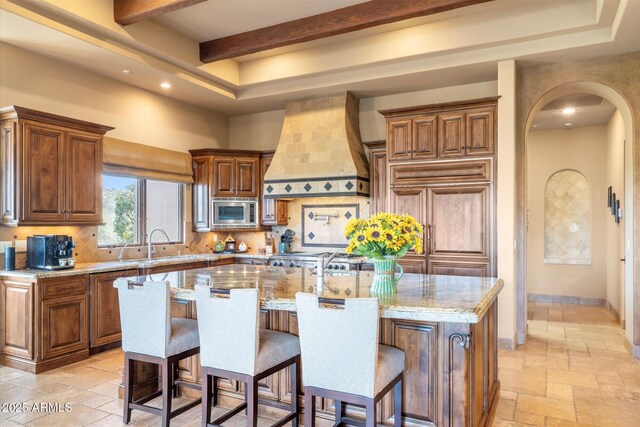 15956 E Tombstone Trl, Fountain Hills, AZ 85268 - kitchen featuring a kitchen island with sink, custom range hood, stainless steel microwave, stone tile floors, and arched walkways