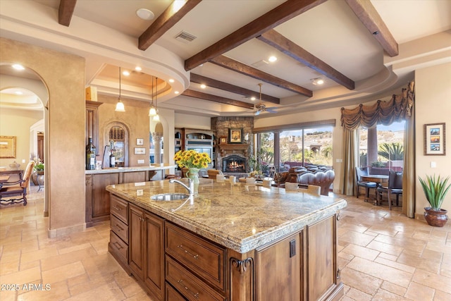 15956 E Tombstone Trl, Fountain Hills, AZ 85268 - kitchen featuring brown cabinetry, visible vents, arched walkways, a sink, and stone tile flooring
