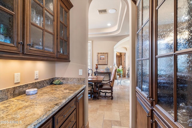15956 E Tombstone Trl, Fountain Hills, AZ 85268 - kitchen with visible vents, arched walkways, glass insert cabinets, and stone tile flooring