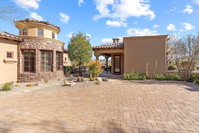 back of property with a tile roof, a patio, stone siding, and stucco siding