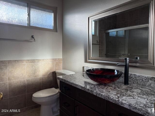 bathroom with walk in shower, vanity, tile walls, and toilet