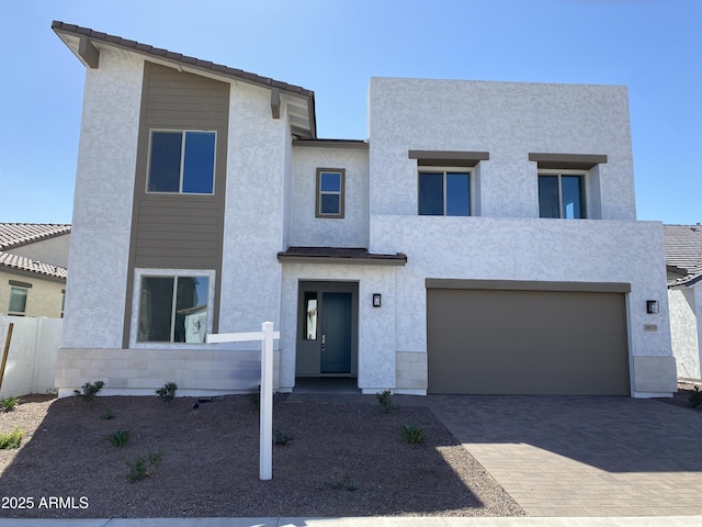 view of front of home with fence, an attached garage, stucco siding, a tile roof, and decorative driveway