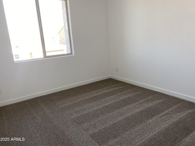 spare room featuring dark carpet and baseboards