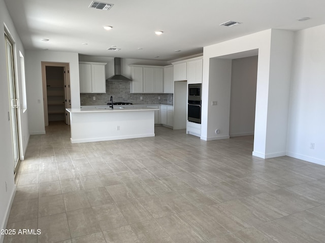 kitchen with visible vents, stainless steel appliances, light countertops, wall chimney exhaust hood, and backsplash