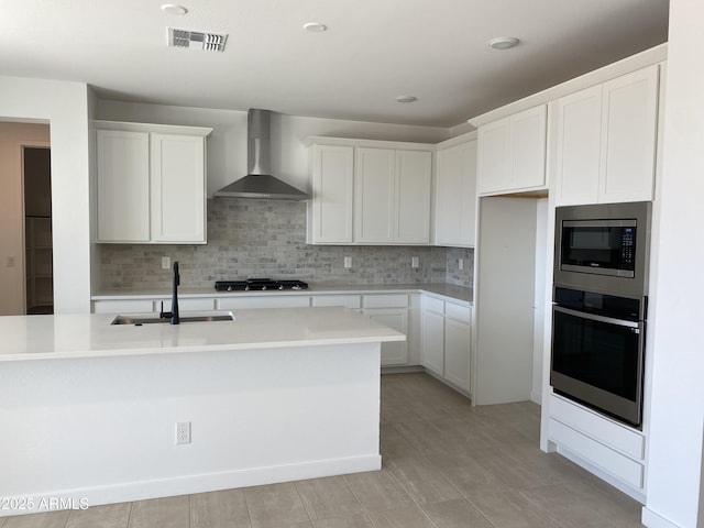 kitchen featuring visible vents, decorative backsplash, appliances with stainless steel finishes, wall chimney exhaust hood, and a sink