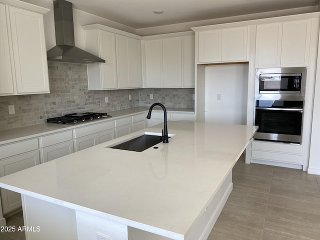 kitchen with tasteful backsplash, wall chimney range hood, white cabinets, stainless steel appliances, and a sink