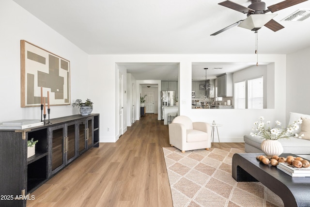 living room with visible vents, ceiling fan, baseboards, and light wood-style floors