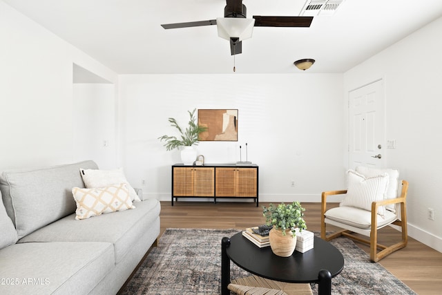 living room featuring ceiling fan, visible vents, baseboards, and wood finished floors