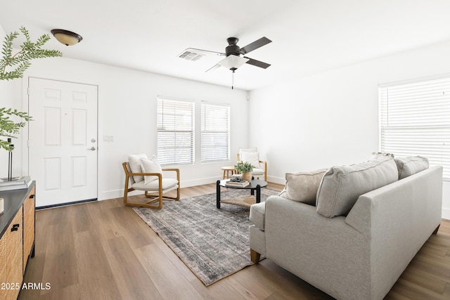 living room featuring ceiling fan, visible vents, baseboards, and wood finished floors