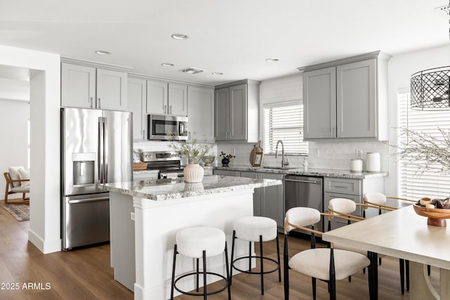 kitchen with gray cabinetry, a sink, backsplash, a center island, and stainless steel appliances