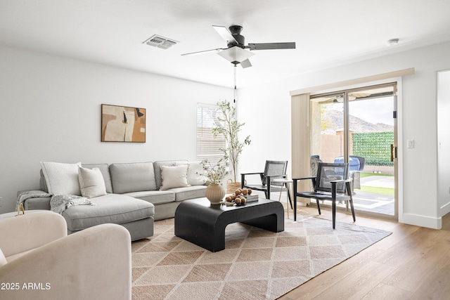 living room with ceiling fan, baseboards, visible vents, and light wood-type flooring