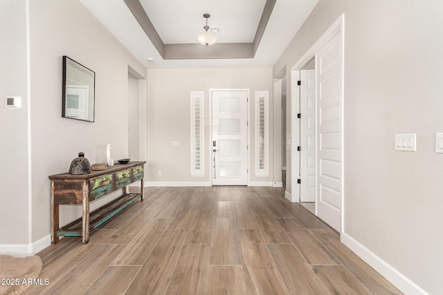 foyer featuring baseboards, a tray ceiling, and light wood-style floors