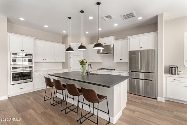 kitchen with a sink, stainless steel appliances, visible vents, and light wood finished floors